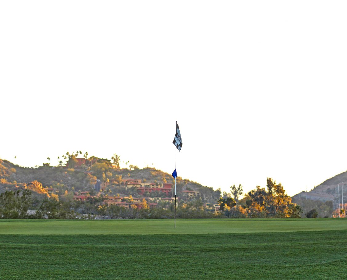 PHXTCPR Golf_Resort1 Golf course with checkered flag pin in the foreground and resort buildings nestled into the mountainside in the background